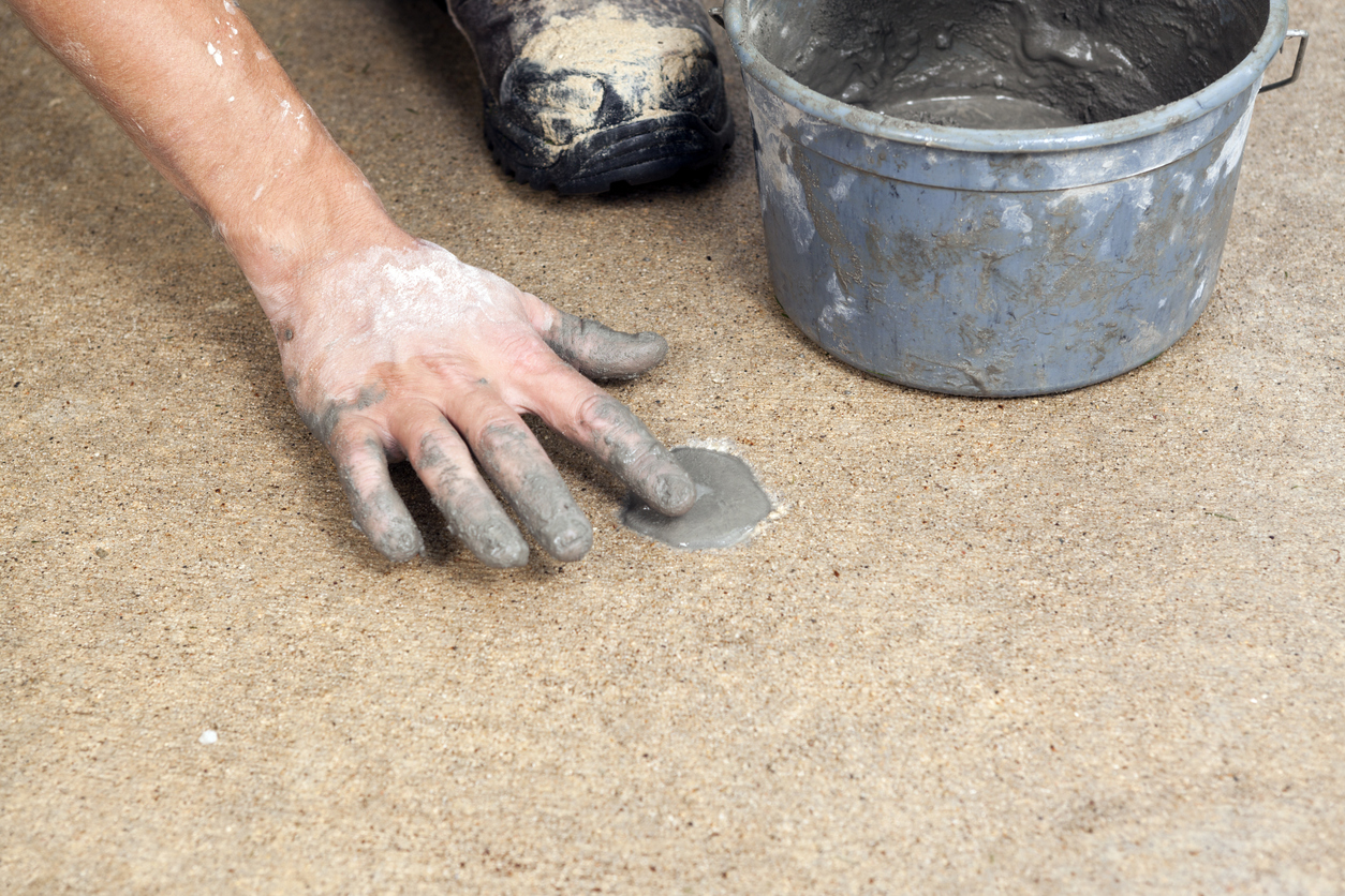 A worker is applying grout to patch a hole drilled in a section of concrete sidewalk which was filled with slurry to raise the panel, a repair technique known as mudjacking.