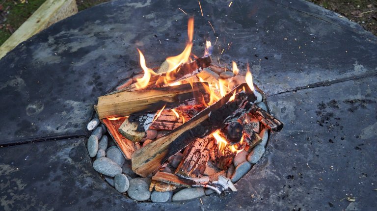 Outdoor fire pit with a round concrete tabletop and fire lit inside.
