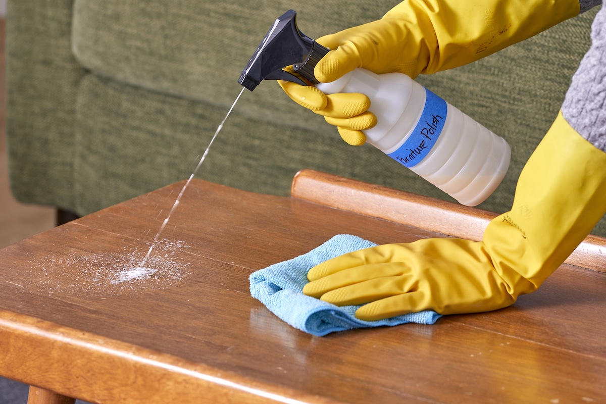 Woman wearing yellow rubber gloves sprays wood coffee table with homemade furniture polish.