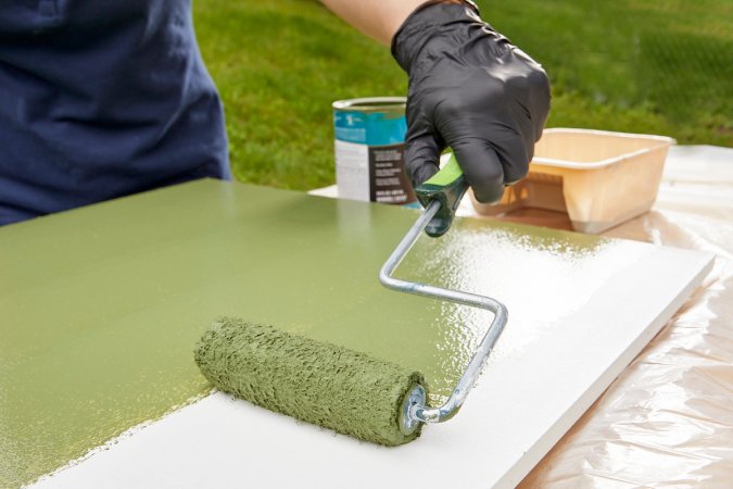 Woman using a roller to paint a piece of white MDF a shade of green.