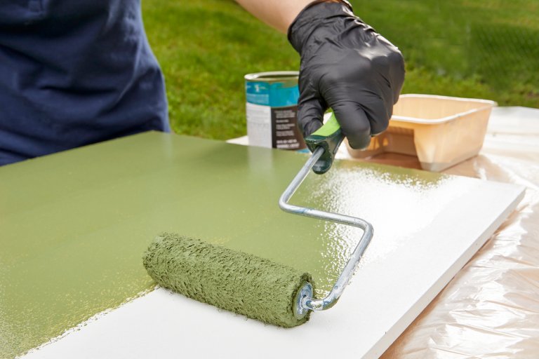 Woman using a roller to paint a piece of white MDF a shade of green.