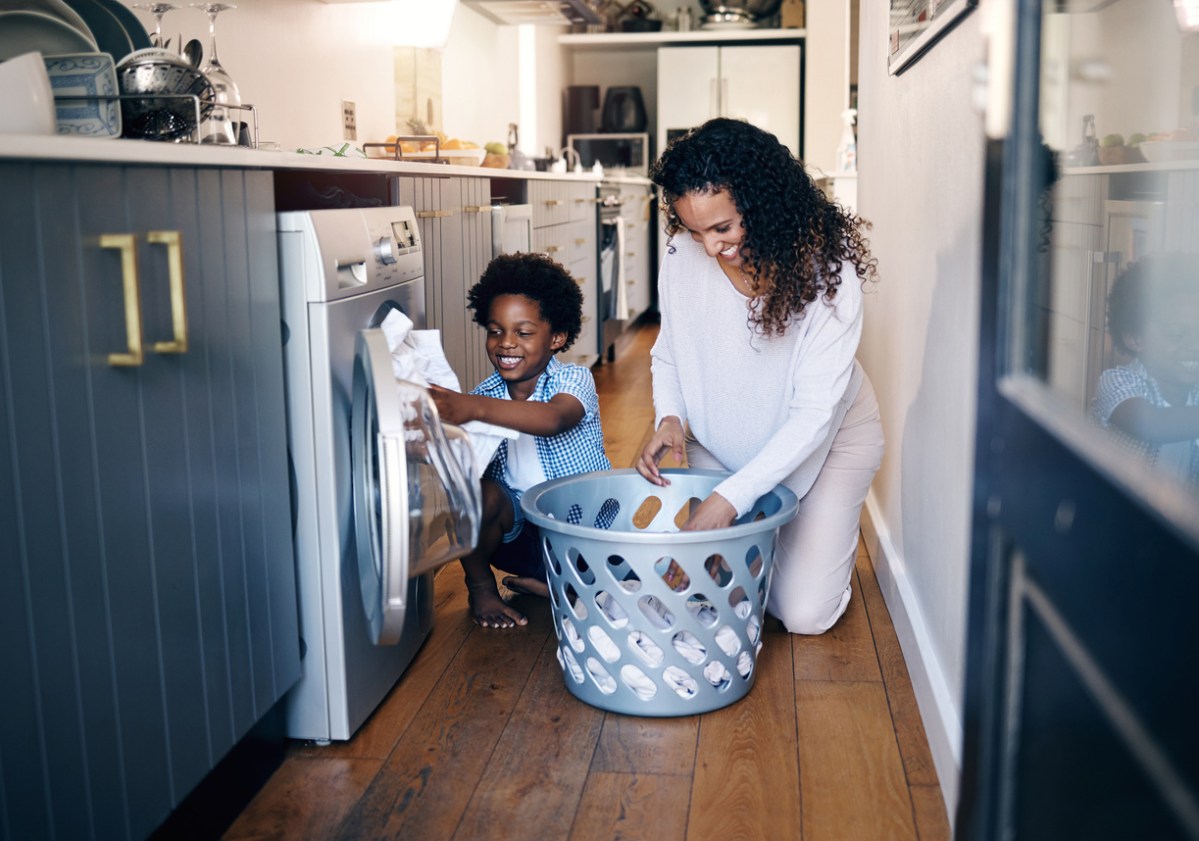 African American boy with an afro smiling and faving fun while doing housework with him mother at home. mixed race shot of a cute child folding laundry with his mom