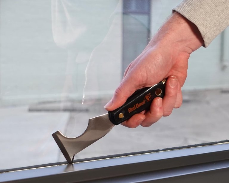 Person holding a Red Devil's 6-in-1 painter's tool against a window sill.