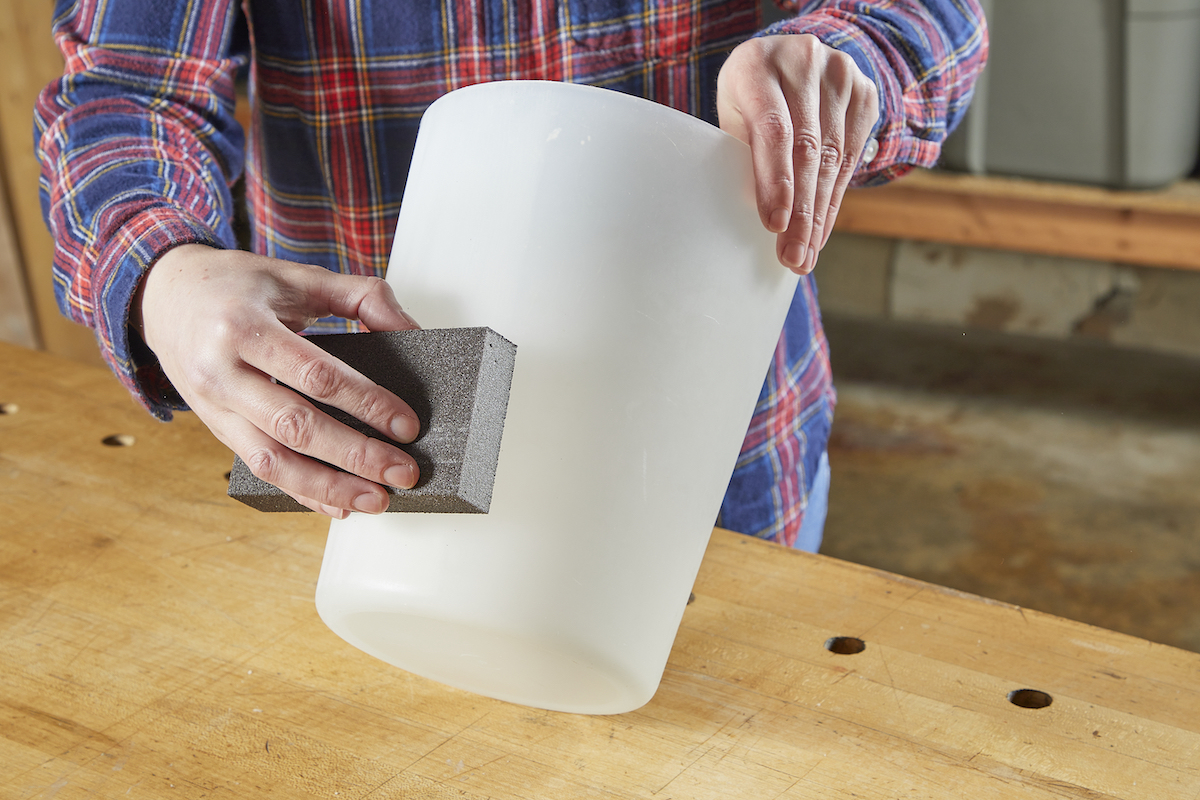 Person using sandpaper to sand plastic bin.