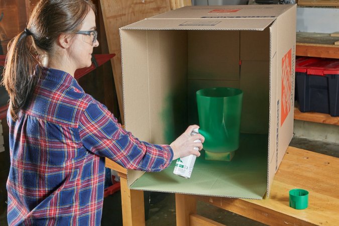 Woman using green spray paint in cardboard box.
