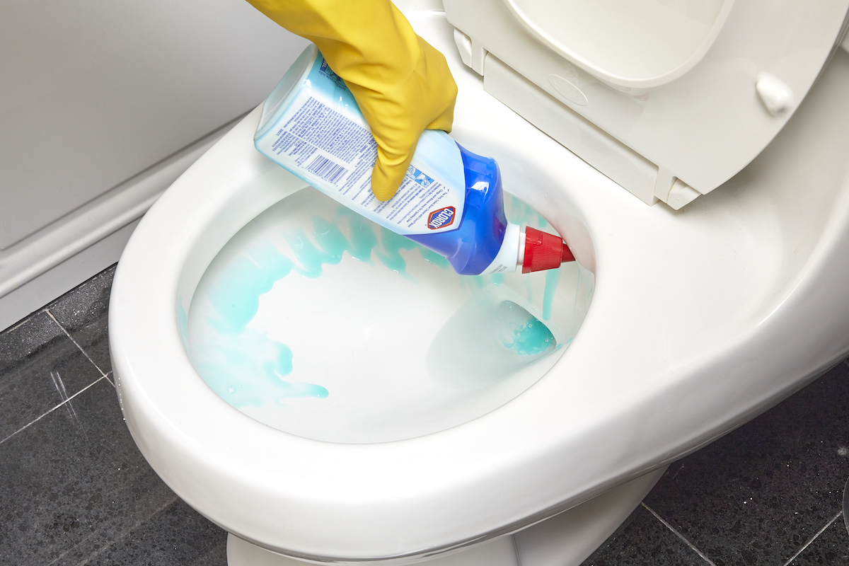 Woman wearing rubber gloves spraying toilet cleaner inside the rim of the toilet.