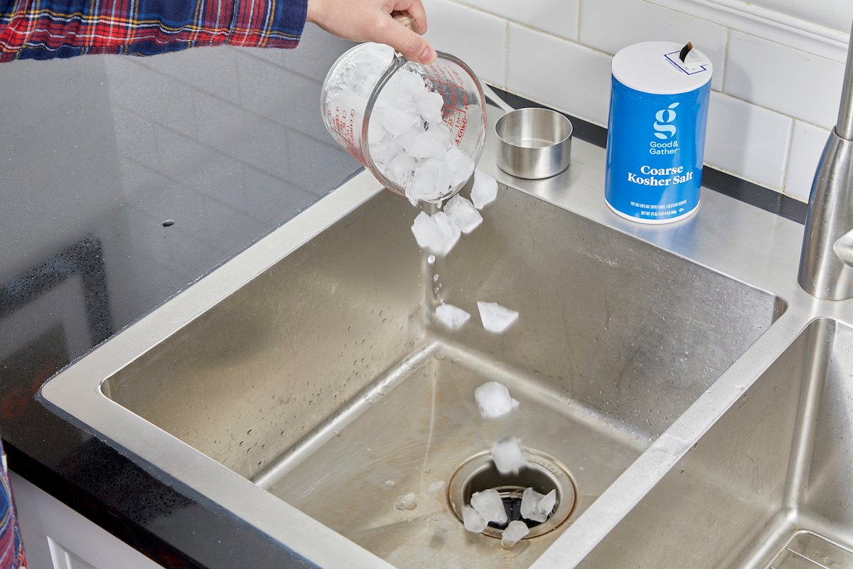 Woman dumps ice cubes into kitchen sink, a container of salt nearby.
