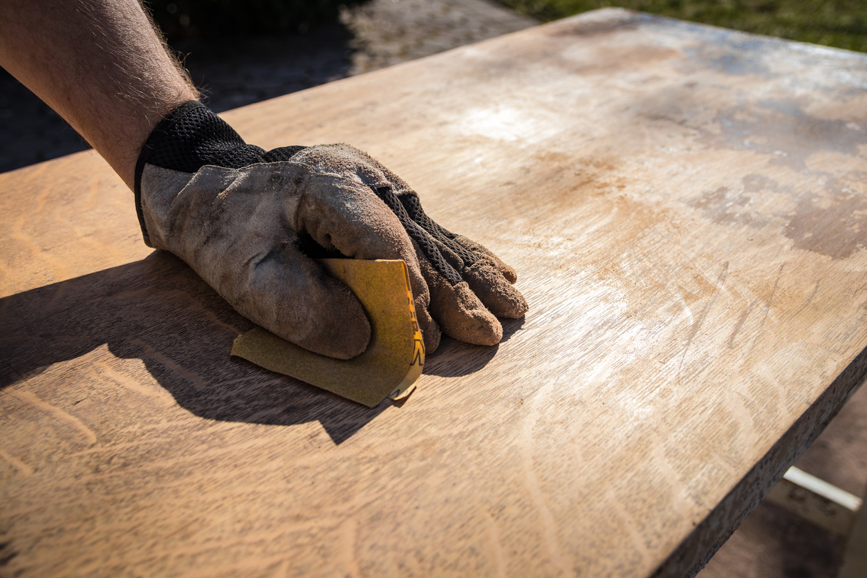 man's hand in work glove using sandpaper to sand wood