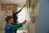 A mother and son scraping off old wallpaper and glue off a bedroom wall.