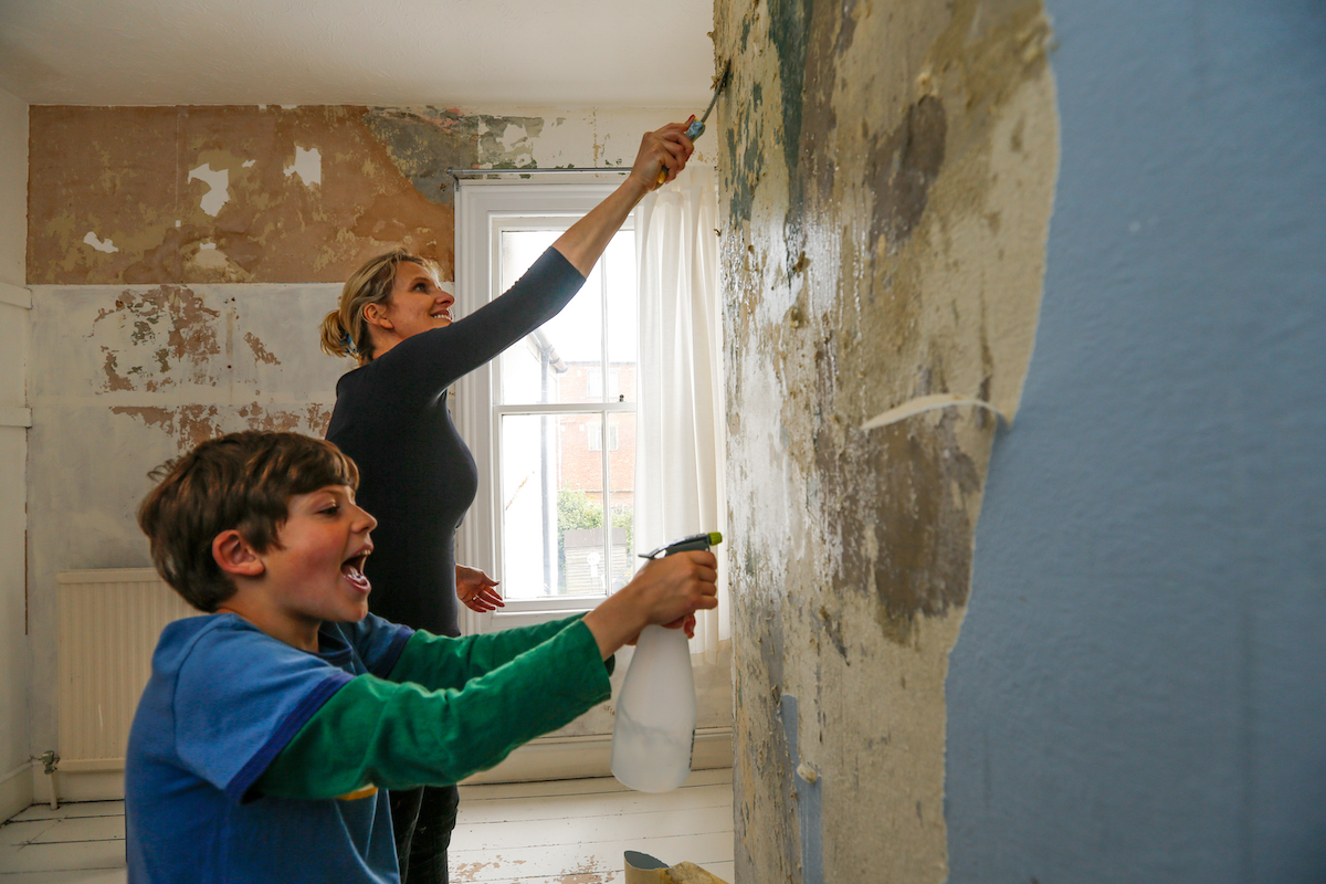 A mother and son scraping off old wallpaper and glue off a bedroom wall.