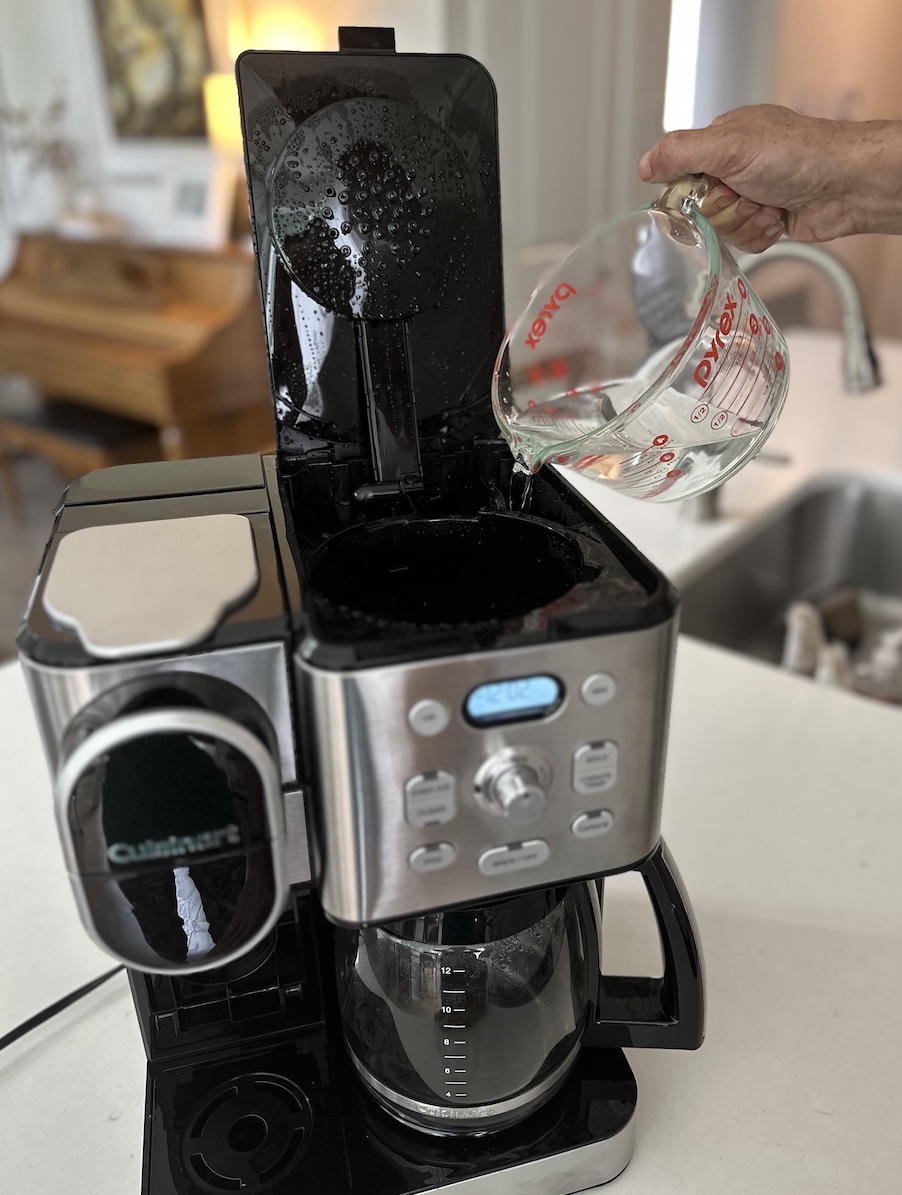 Man pouring water and vinegar into coffee maker reservoir