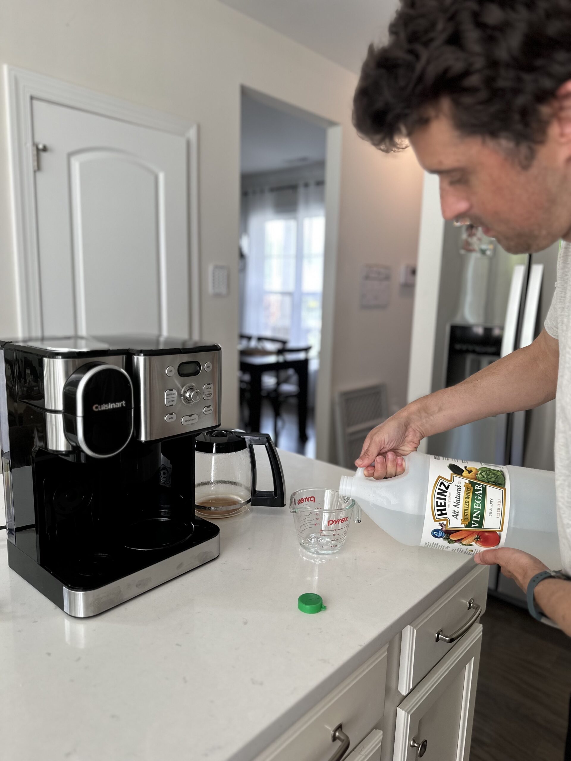the author pouring vinegar into a measuring cup with coffee maker on kitchen counter
