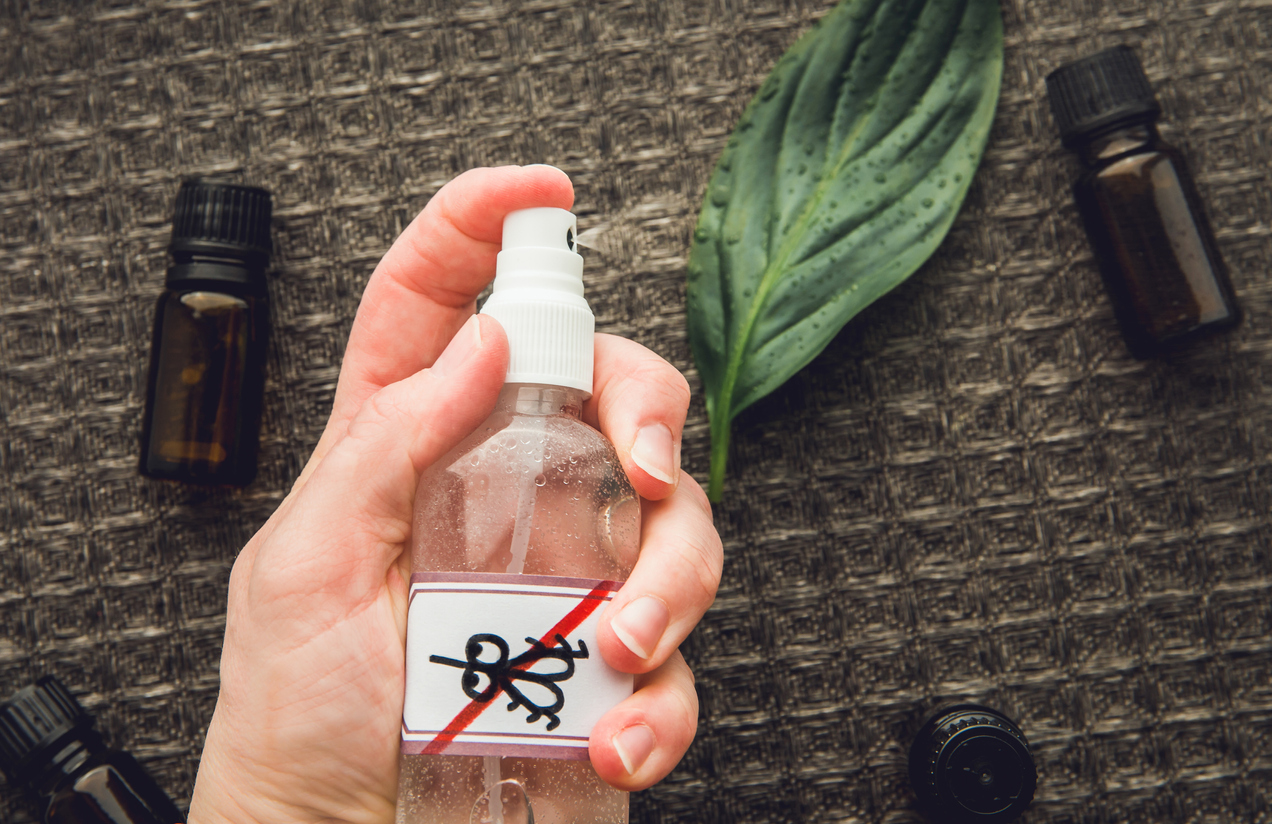 woman's hand holding spray bottle with anti-insect label with bottles of essential oils on the table