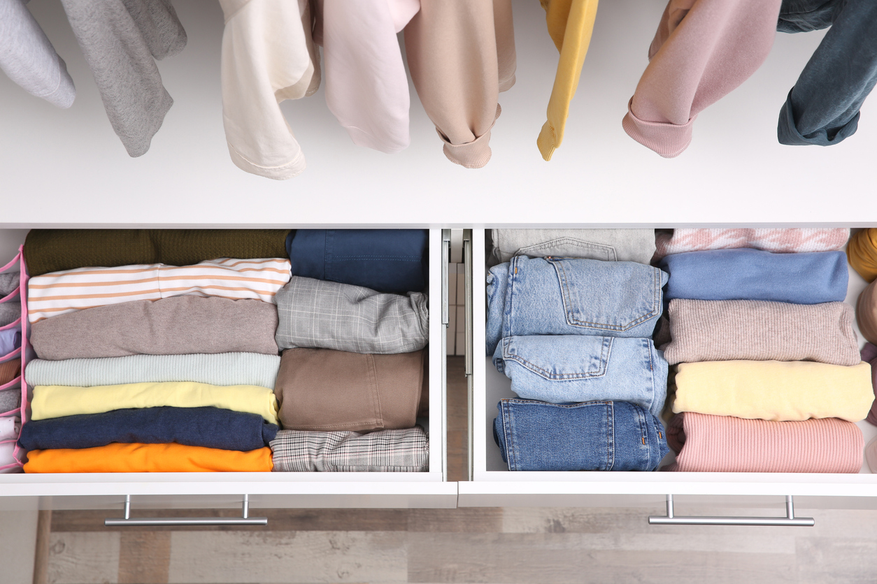 overhead view of wardrobe drawer open with neatly folded clothing inside with clothing hanging above