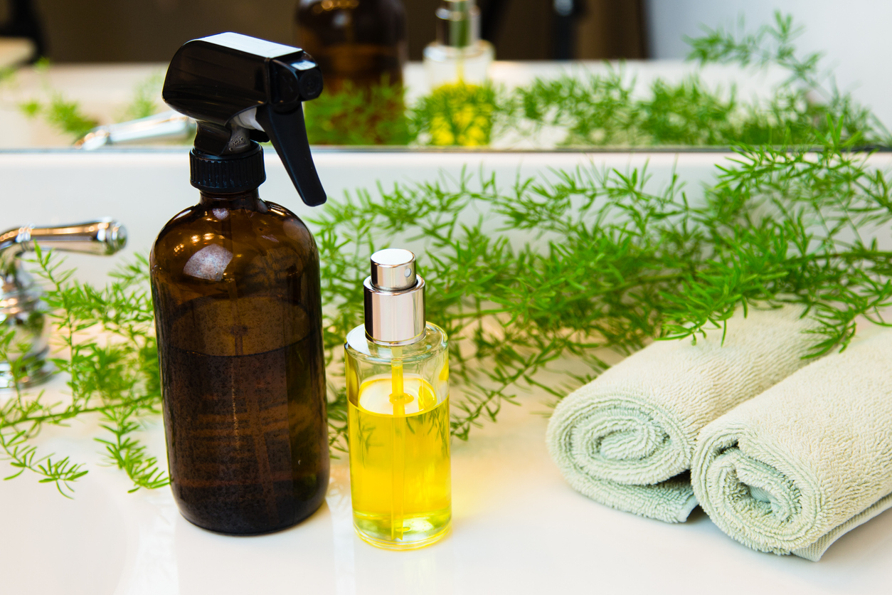 spray bottle and small bottle of essential oils on bathroom counter next to rolled up hand towels with decorative plant vines in front of mirror
