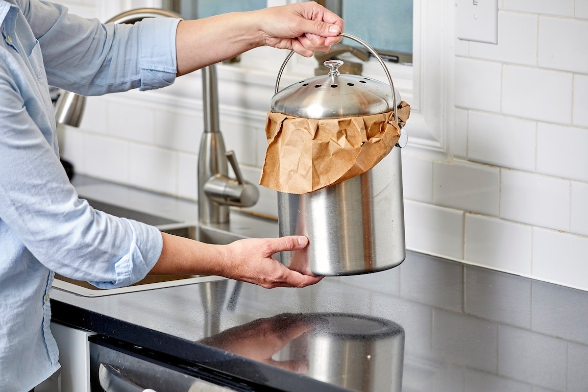 Woman places a stainless steel compost bin on a kitchen countertop.