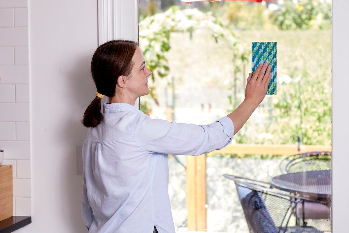 Woman stands by sliding glass door and hangs a piece of fly paper on the glass.