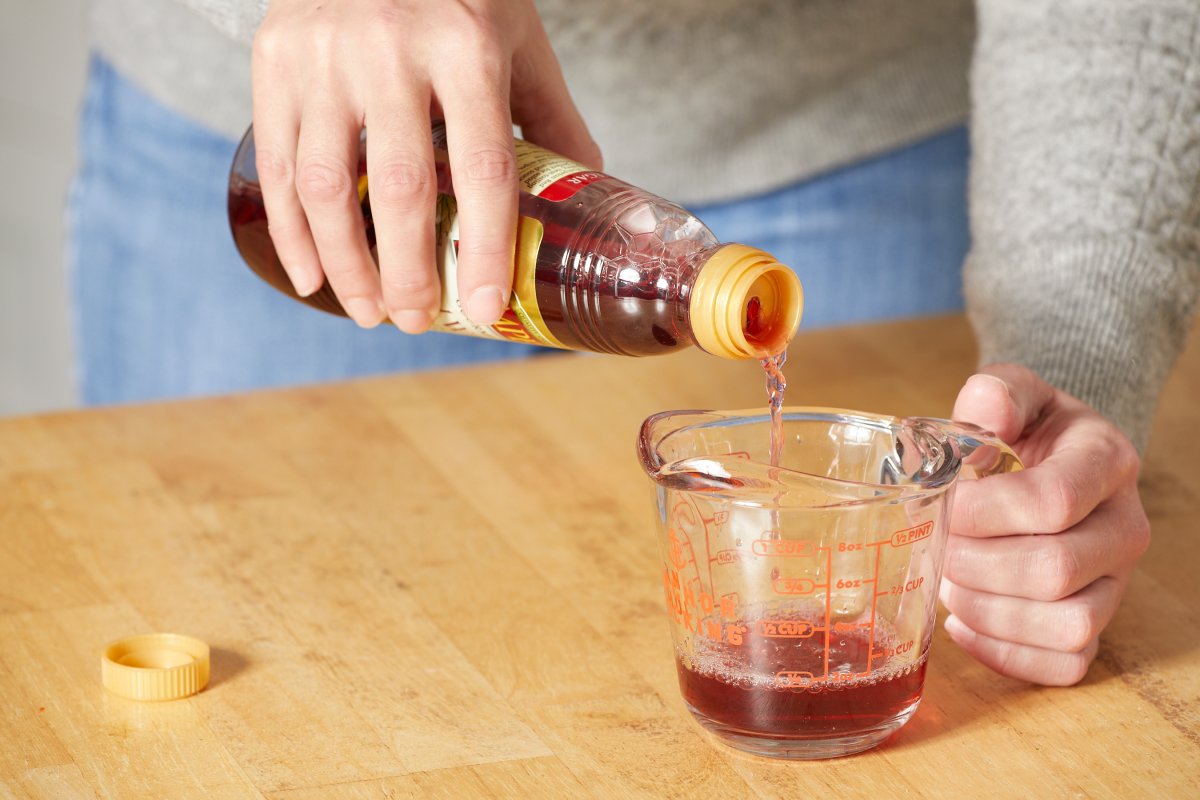 Woman pours red wine vinegar into a glass measuring cup.
