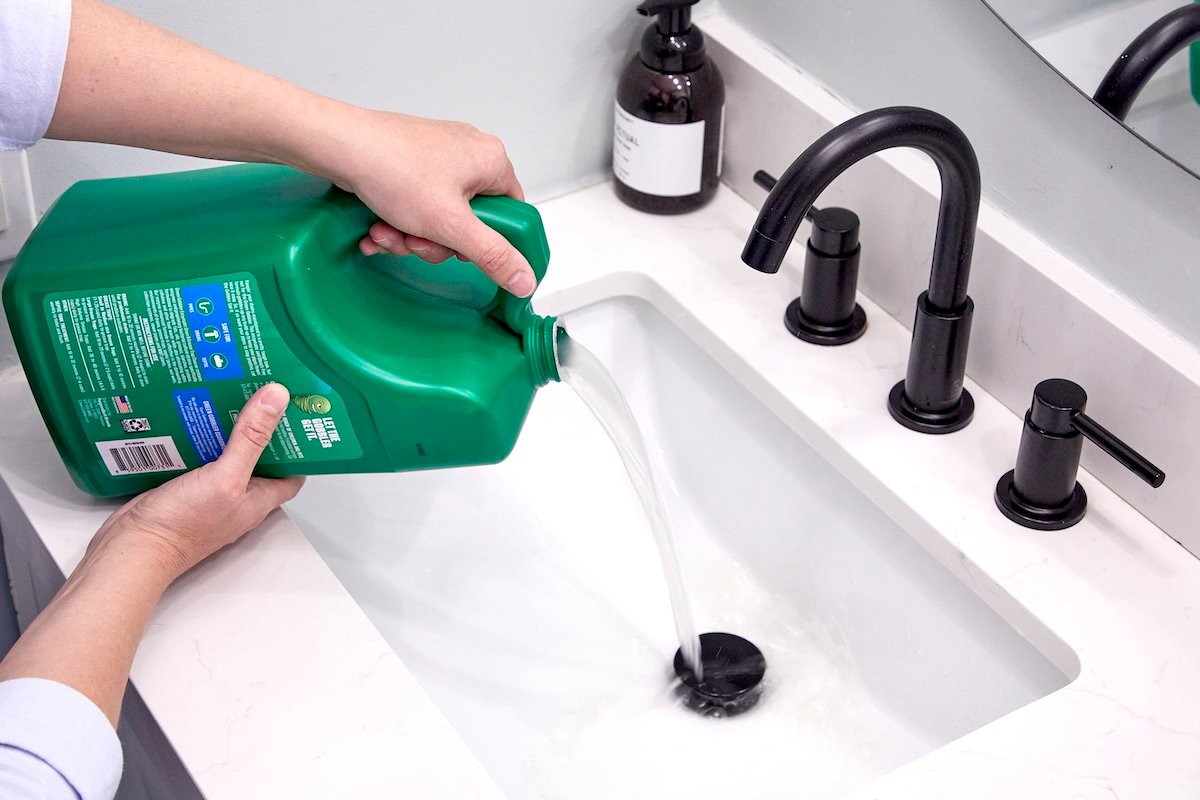 Woman pours enzyme cleaner into a bathroom sink drain.