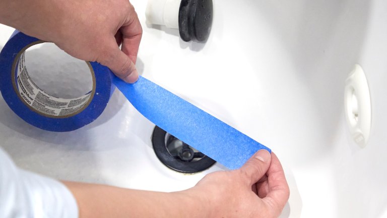 Woman pulls a piece of painter's tape off a roll and prepares to place it over a tub drain.