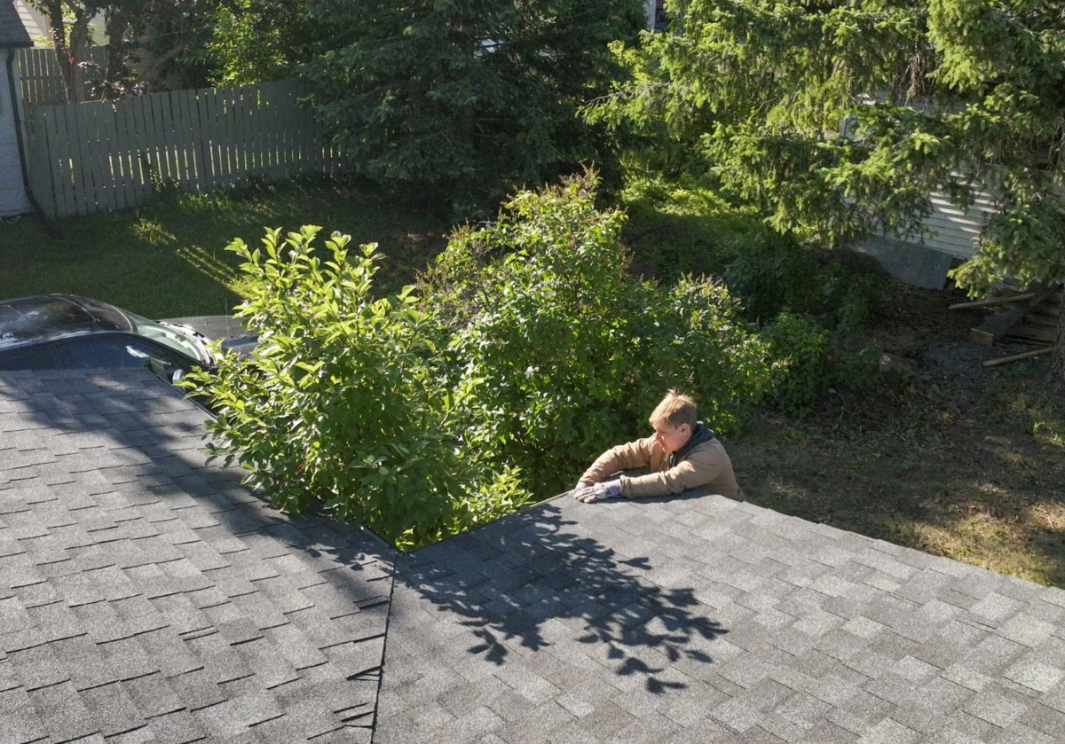 A young man removing tree branches and leaves from roof.