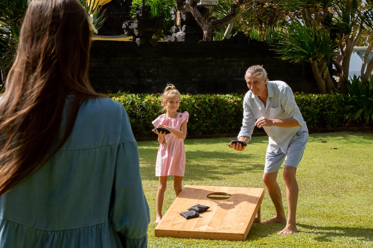 Family playing cornhole game outdoor on sunny summer day. Parents and children playing bean bag toss