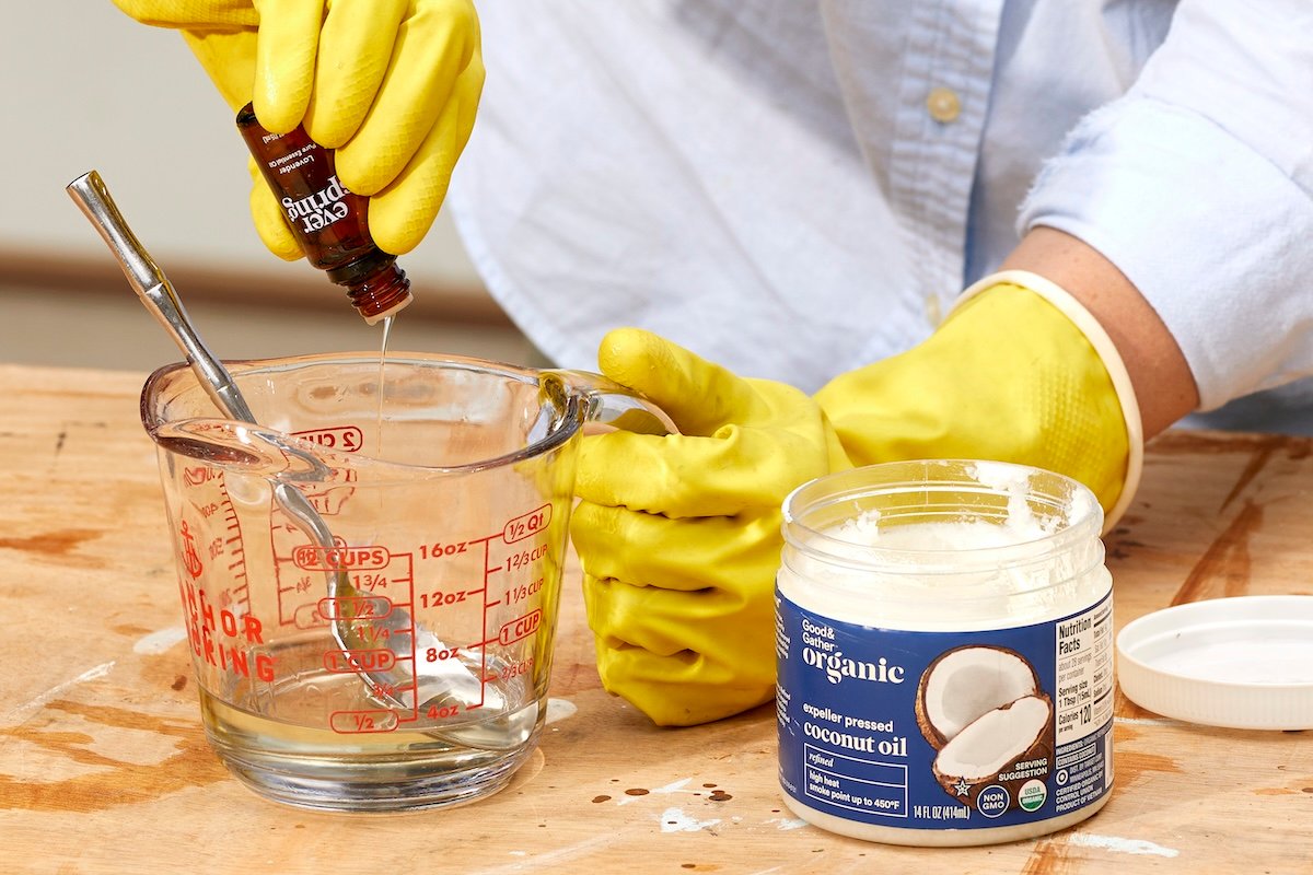 Woman squeezes essential oils into a measuring cup with a jar of coconut oil nearby.