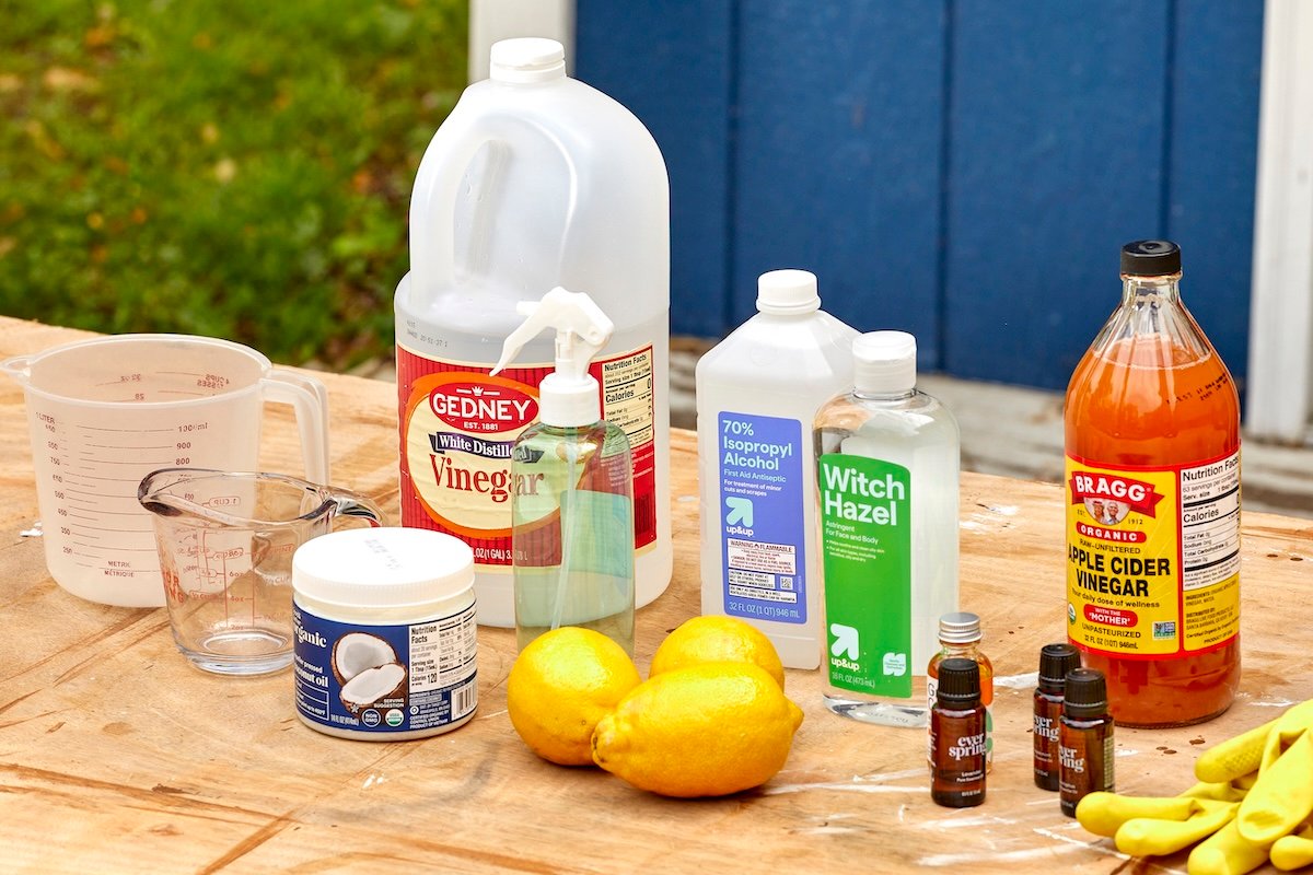 A wood table topped with ingredients such as essential oils, vinegar, lemons, coconut oil and others for making homemade mosquito repellants.