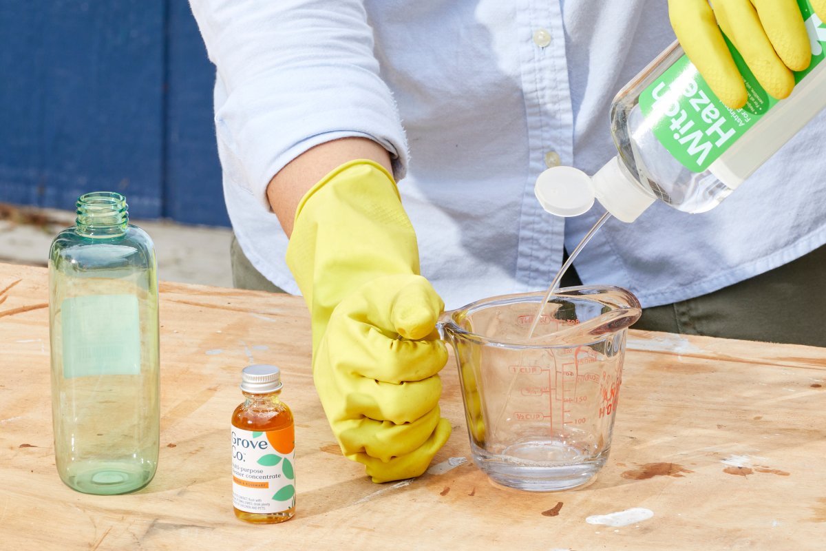 Woman squirts witch hazel into a measuring cup as she makes homemade mosquito repellent.
