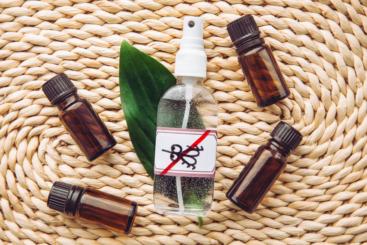 Homemade essential oil based mosquito repellent. Flat lay view of spray bottle surrounded by brown essential oil bottles on bamboo mat background.