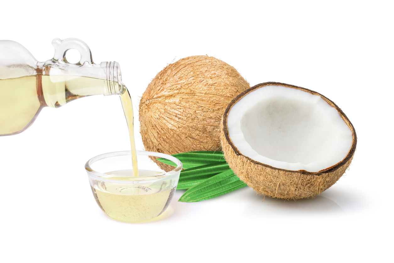 Coconut oil in glass bottle and coconut fruit with green leaves isolated on white background.