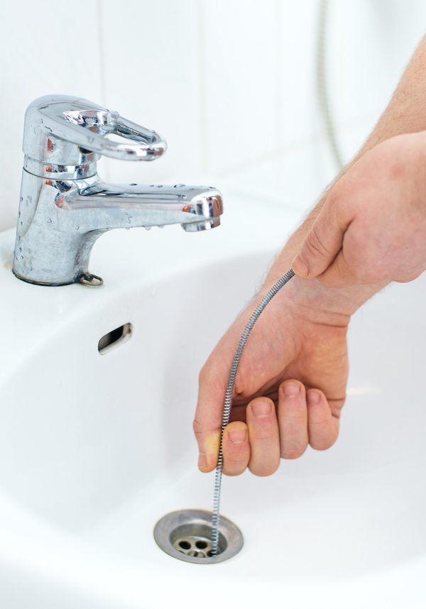 person using drain snake to clear bathroom sink clog