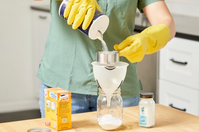 Woman wearing cleaning gloves pours salt through a funnel into a mason jar.