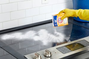 Woman sprinkles a glass cooktop with baking soda.