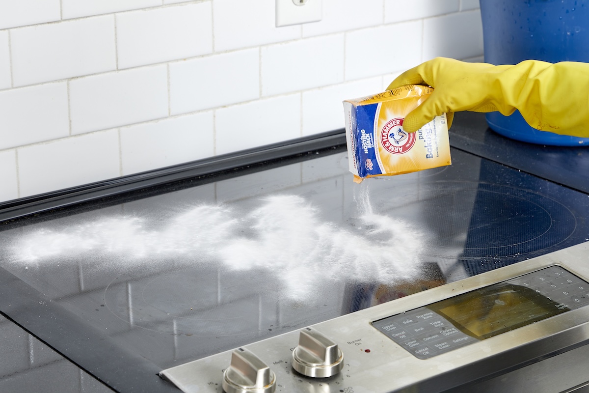 Woman sprinkles a glass cooktop with baking soda.