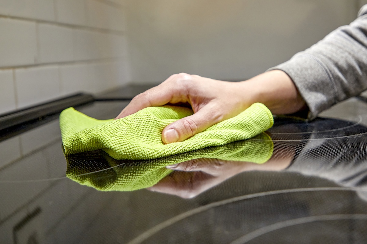 Woman uses a green microfiber cloth to wipe a glass cooktop.