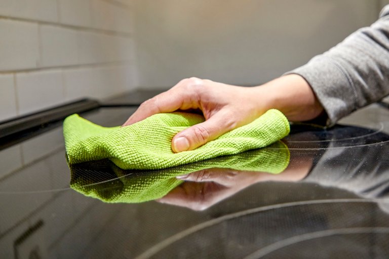 Woman uses a green microfiber cloth to wipe a glass cooktop.