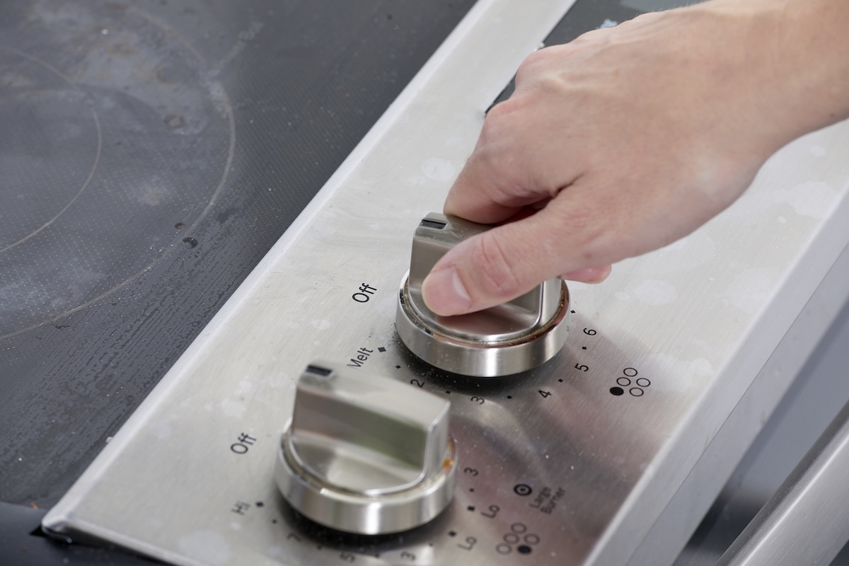 The woman turns the knob on the glass stove.