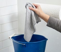 Woman drops a microfiber rag in a blue bucket on top of a stovetop.