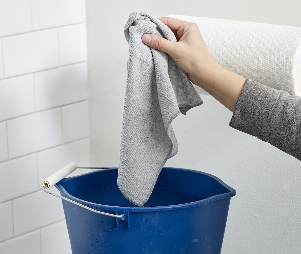Woman drops a microfiber rag in a blue bucket on top of a stovetop.