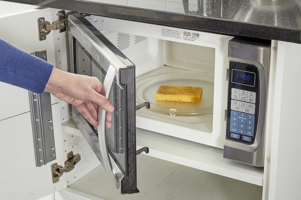 Woman puts yellow dish sponge inside the microwave.