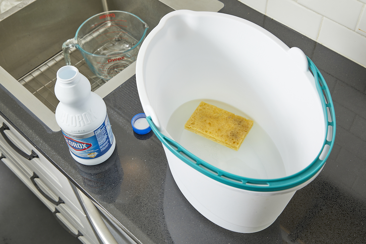 Soaking a yellow dish sponge in a bucket of a bleach solution.