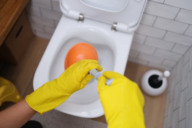 how to use a plunger gloved hands hold plunger over toilet