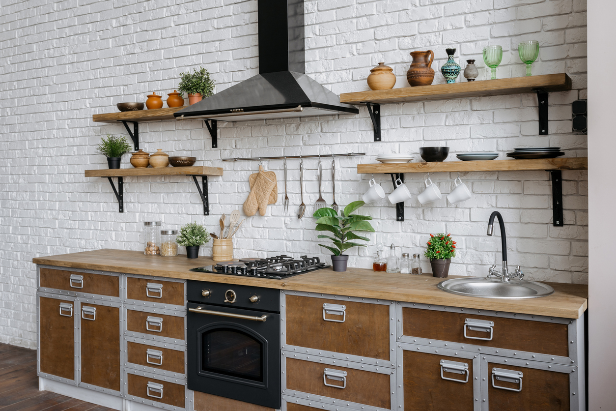 Kitchen with white painted brick walss, natural cabinets and open shelves, with modern range hood.