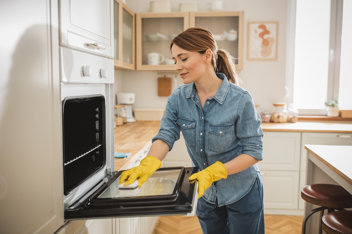 A young woman scrubs the insider of her oven door.