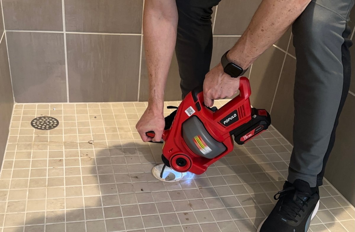 Man stands in shower stall with drain cover removed from shower and drains into drain.