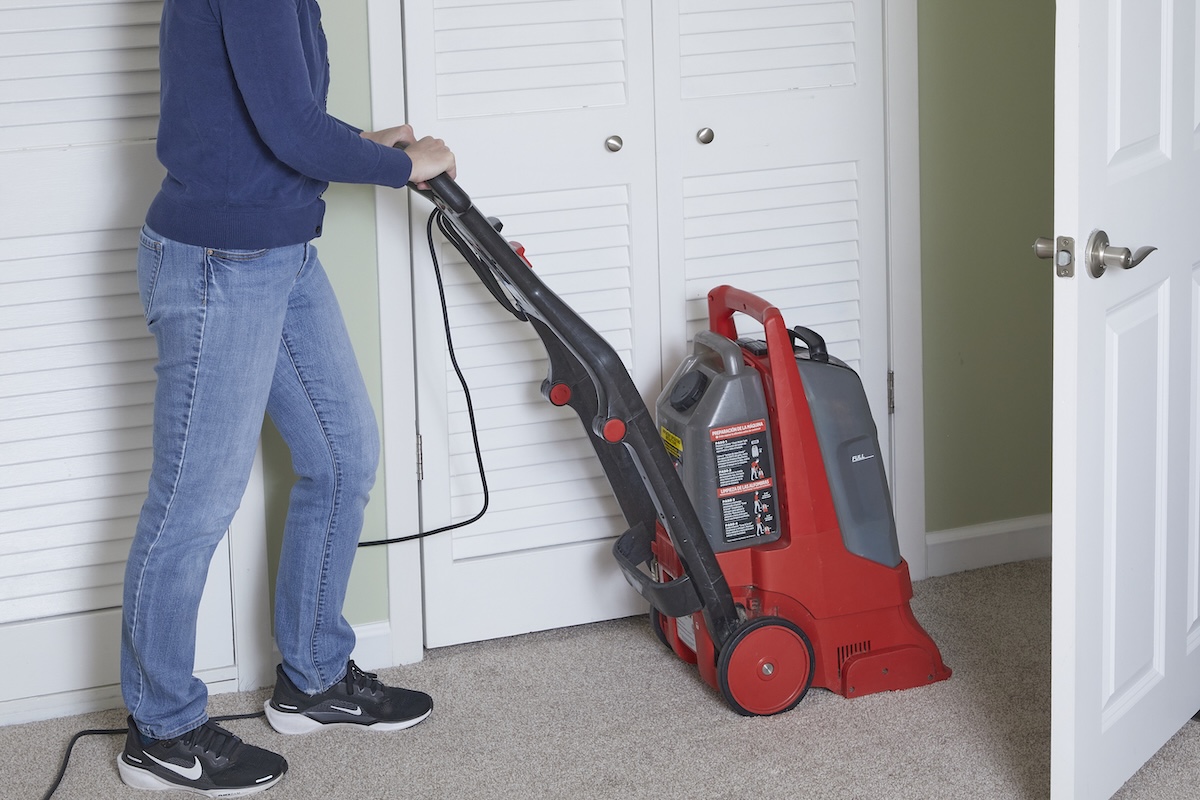 Woman pushes a red carpet cleaning machine through beige carpeting in front of bifold closet doors.