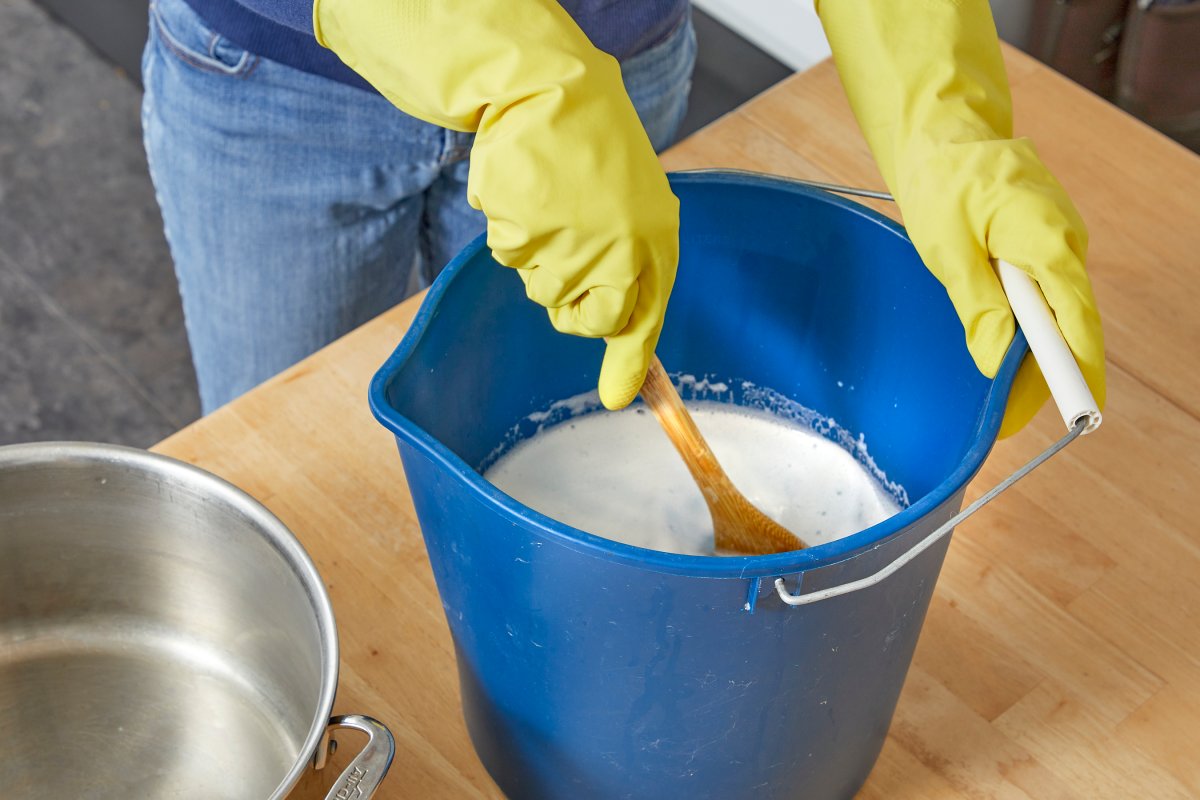 Woman wearing rubber gloves stirs a bucket full of ingredients for homemade carpet cleaning solution.