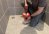 Man crouches in shower with a drain auger poised over the shower drain.