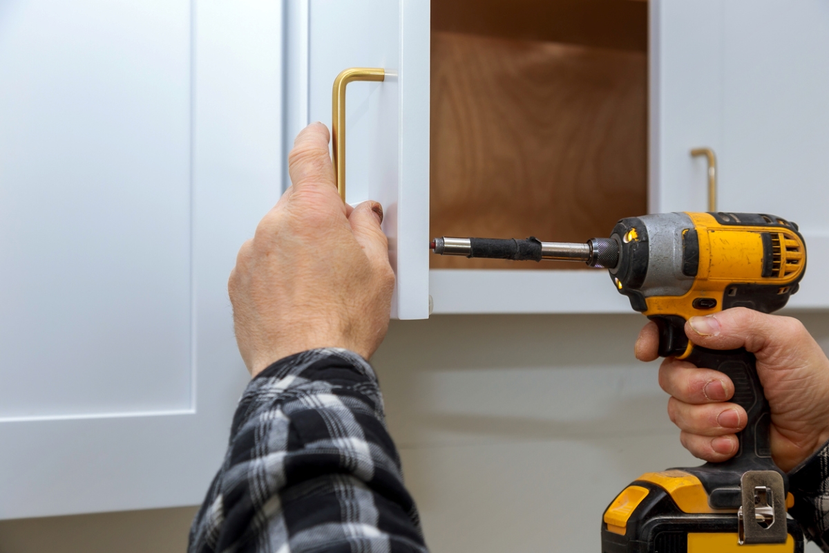 Male hands using drill to remove cabinet handle